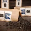 Several brown paper bags of tea are shown, with one bag spilling its contents onto a wooden surface. Produktbild-Vorschau