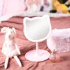 A pink cat-shaped makeup mirror with LED lights is placed on a pink textured surface, next to a stuffed animal and a perfume bottle. Voir les images du produit