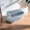 Two transparent storage boxes for boots are stacked on a wooden floor, with shadows cast on a white wall behind them. Produktbild-Vorschau