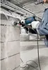 A person is using a Bosch hammer drill to make a hole in a concrete block wall. Anteprima dell’immagine prodotto
