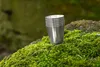 A metal cup sits on a moss-covered rock in a forest setting. Náhled obrázku produktu