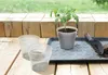 A tomato plant is being repotted on a wooden surface with gardening tools and extra pots. Produktbild-Vorschau