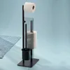 A black toilet brush and toilet paper holder stand with two rolls of toilet paper against a light blue background. Voir les images du produit