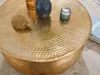 A close-up view of a round, hammered gold coffee table with decorative items on it. Produktbild-Vorschau