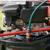 A close-up view of a lawnmower engine with a green hose attached, suggesting a cleaning function. Produktbild-Vorschau