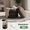 A brown ottoman with a blanket and pillows inside, shown in a living room setting. A smaller version of the ottoman is shown in the bottom left corner with a teddy bear and pillows. Produktbild-Vorschau