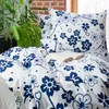 A close-up view of a bedding set with a floral pattern, placed on a bed near a window with plants. Produktbild-Vorschau