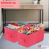 Two pink storage boxes filled with toys and books are placed on a light gray surface in front of a desk. Produktbild-Vorschau