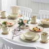 A beautifully set dining table with a complete porcelain dinnerware set for four people, including plates, bowls, and mugs, arranged for a meal. Náhled obrázku produktu