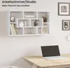 A white wall-mounted shelf unit filled with decorative items and books, above a wooden desk with a laptop. Produktbild-Vorschau