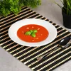 A bowl of tomato soup garnished with basil and drizzled with oil, placed on a black and beige placemat. Náhľad obrázku produktu