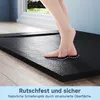 A person's feet are shown stepping onto a black, textured shower tray with a slate-like appearance, highlighting its non-slip surface. Produktbild-Vorschau