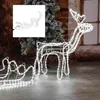 A white wireframe reindeer with a sleigh, illuminated by white LEDs, stands in front of a Christmas tree. Produktbild-Vorschau