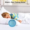 A young boy is sleeping peacefully in bed next to a blue alarm clock. Produktbild-Vorschau