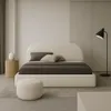 A minimalist bedroom with a large upholstered bed, a side table with a vase, and a floor lamp. Náhled obrázku produktu