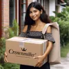 A woman is holding a package with the 'Crownmiller' logo on it, with a large bag slung over her shoulder. She is standing outside a building with greenery in the background. Produktbild-Vorschau