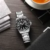 A watch is placed on a wooden table next to some newspapers and a cup of tea. Produktbild-Vorschau