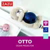 A baby is lying next to a stuffed otter toy that projects ocean-like lights and sounds. Produktbild-Vorschau