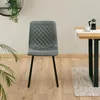 A gray quilted dining chair with black legs is placed on a wooden floor next to a dining table with a French press and a cup of coffee. Produktbild-Vorschau