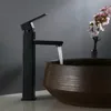 A black faucet is shown running water into a brown basin, with a vase of pink flowers in the background. Náhľad obrázku produktu