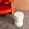 A cream-colored side table is placed on a speckled floor next to an orange chair. Anteprima dell’immagine prodotto