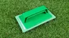 A green cleaning pad with a green handle rests on a patch of artificial grass. Produktbild-Vorschau