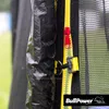 Close-up view of a black trampoline safety net with a yellow zipper and a red zipper pull, along with a black buckle. The BullPower logo is visible in the bottom right corner. The background shows out-of-focus green grass and a light blue structure. Produktbild-Vorschau