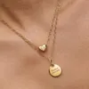 A close-up shot of a person wearing two gold necklaces with pendants. Anteprima dell’immagine prodotto