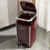 A red pedal trash can with its lid open, placed on a tiled floor next to a cabinet and sheer curtains. Produktbild-Vorschau