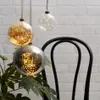Three decorative glass spheres with internal LED lights hang in front of a white brick wall and a black chair. Podgląd zdjęcia produktu
