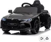 A black electric toy car, resembling a BMW M4 Competition, is shown from a front-side angle against a white background. A white remote control is visible in the bottom right corner. Anteprima dell’immagine prodotto