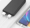 A black power bank with a carbon fiber texture is shown charging a tablet and a smartphone. Produktbild-Vorschau