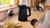A black Bosch electric kettle is shown on a kitchen counter with close-up views of its features. Podgląd zdjęcia produktu