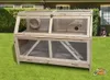 A wooden pet cage with multiple levels and accessories, placed on a green lawn in front of a house. Produktbild-Vorschau