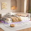 A modern white upholstered corner bed with decorative pillows and throws, set in a bedroom with soft lighting and a wall niche containing a lamp. Náhľad obrázku produktu