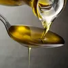 Olive oil being poured from a bottle into a spoon. Produktbild-Vorschau