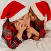 Two children wearing Santa hats and plaid pajamas are lying in bed. Podgląd zdjęcia produktu