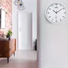 A hallway with a wooden cabinet, a plant, and a white wall clock. Anteprima dell’immagine prodotto