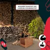 A wicker basket for firewood is placed on a patio in front of a large stack of firewood and some greenery. Náhľad obrázku produktu