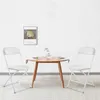 Two white folding chairs are placed on either side of a small wooden table, set against a plain white wall. Anteprima dell’immagine prodotto