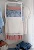 A closet with hanging and folded clothing, including jeans, skirts, and a t-shirt, displayed on a hanger and shelf. Anteprima dell’immagine prodotto