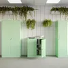 A modern office setting with green metal cabinets and hanging plants. Podgląd zdjęcia produktu