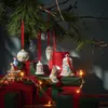 Christmas ornaments hanging from a pine branch above wrapped gifts and fairy lights. Anteprima dell’immagine prodotto