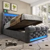 A grey upholstered storage bed with the mattress lifted, revealing storage space underneath. Blue LED lighting is visible along the base and headboard. Produktbild-Vorschau