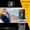An elderly woman on a beach is using a flip phone, with a picture of a young woman displayed on the phone's screen and in a small inset box above. The phone is a "bea fon SL605". Voir les images du produit