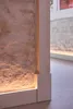 Close-up of a white baseboard and a textured stone wall with integrated lighting. Produktbild-Vorschau