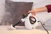 A hand is holding a white steam cleaner and using it on a grey cushion. Podgląd zdjęcia produktu