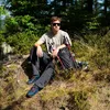 A young man sits on a rocky, wooded trail with a backpack and hiking poles. Náhľad obrázku produktu