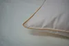 A close-up of a pillow with a beige trim, lying on a white surface. Produktbild-Vorschau