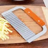 A wavy-bladed knife with a wooden handle rests on a wooden cutting board next to shredded potatoes. Produktbild-Vorschau